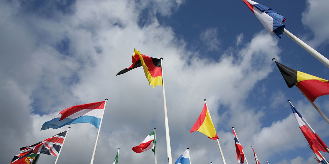 Group of flags of many different nations against blue sky