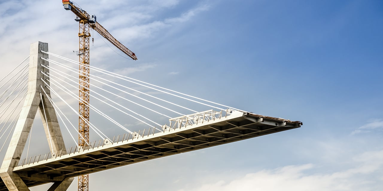 Partially constructed cable-stayed bridge with a crane against a blue sky.