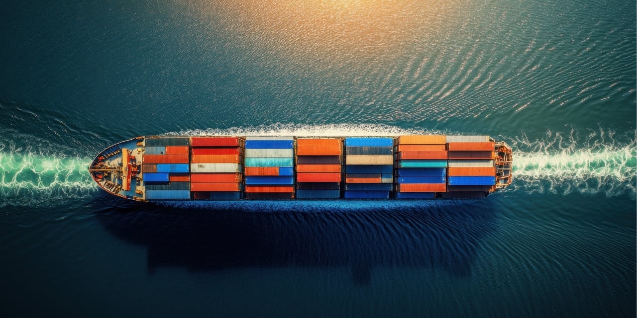 Cargo ship with colorful containers sails through calm blue water, leaving a white wake behind.