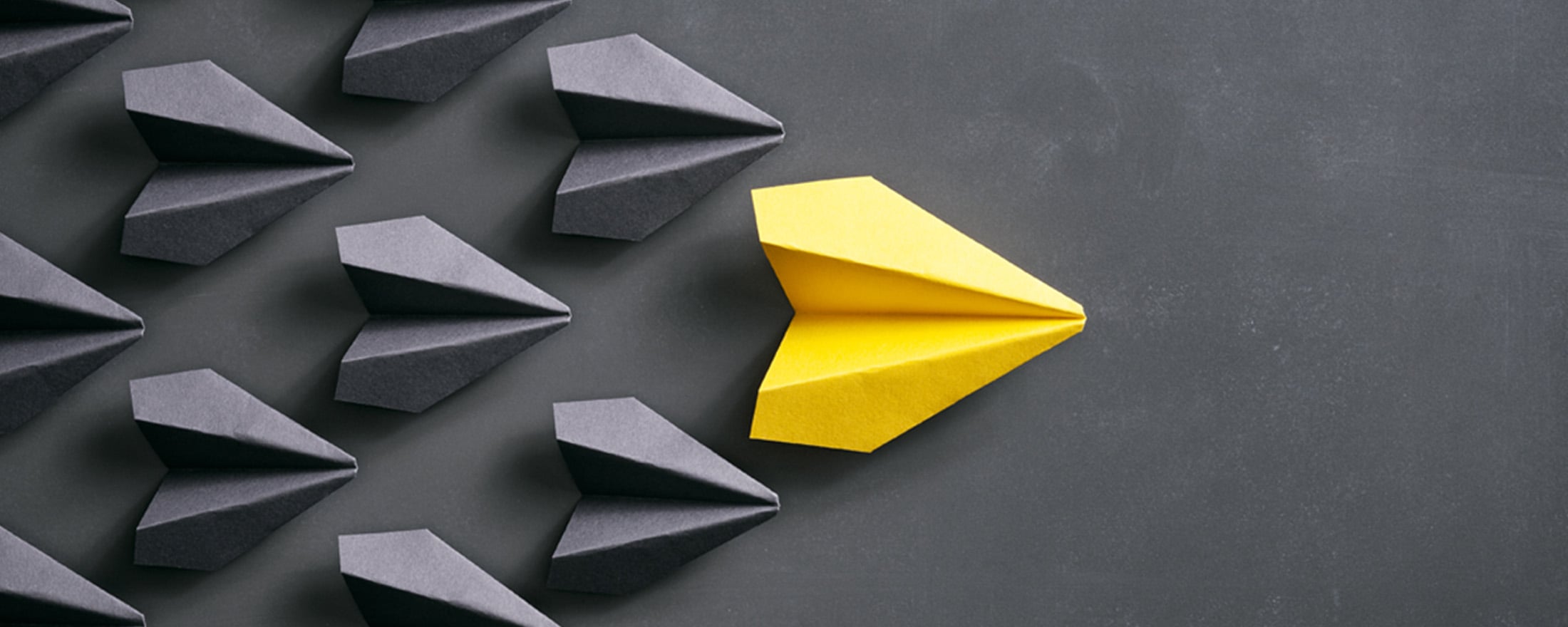 Yello paper airplane in a pyramid with grey paper airplanes
