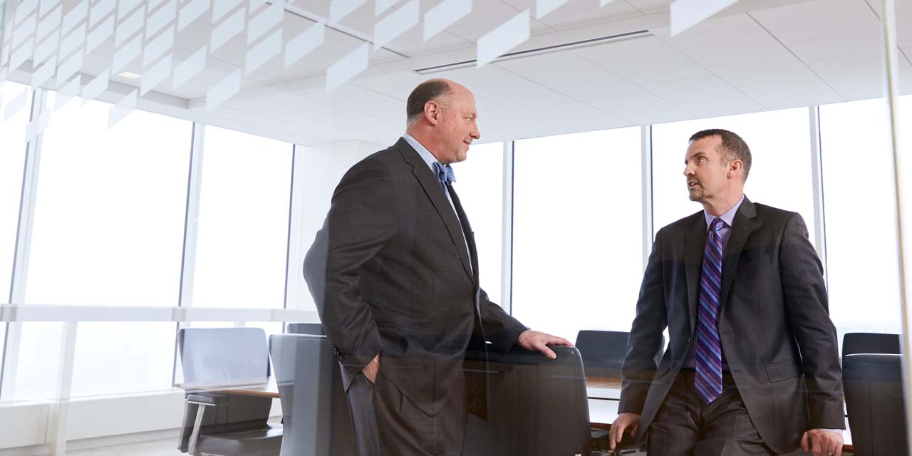 Two men in suits talking in a conference room.