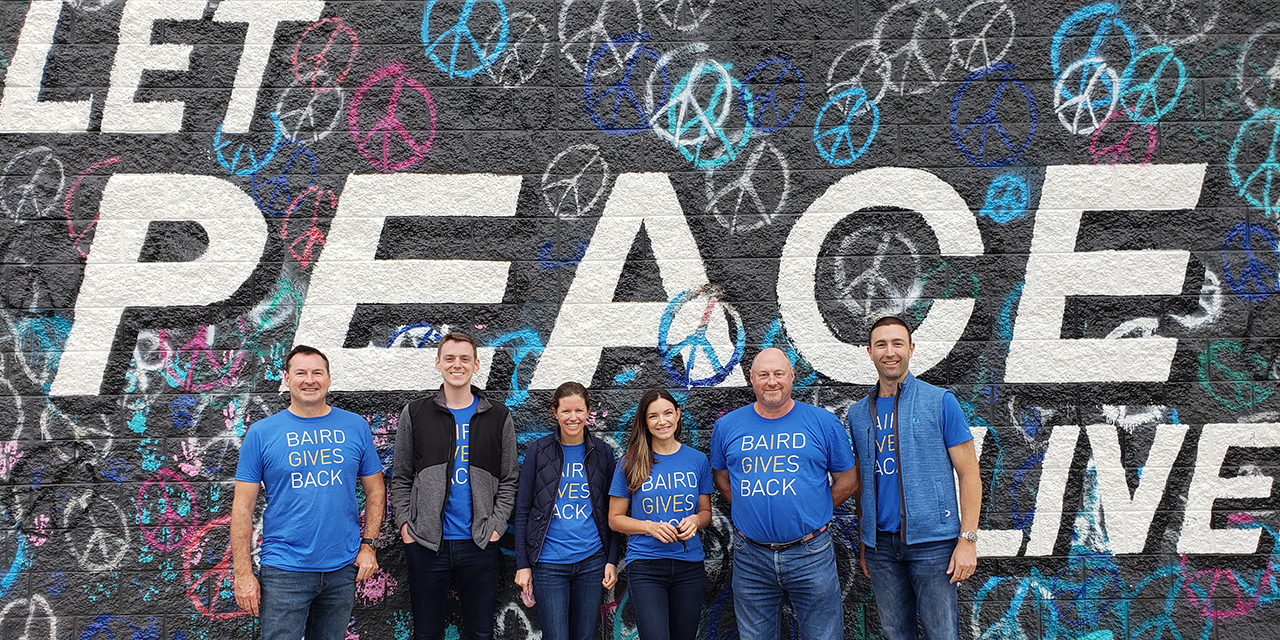 Six Baird associates standing in front of a painted wall wearing Baird Cares t-shirts.