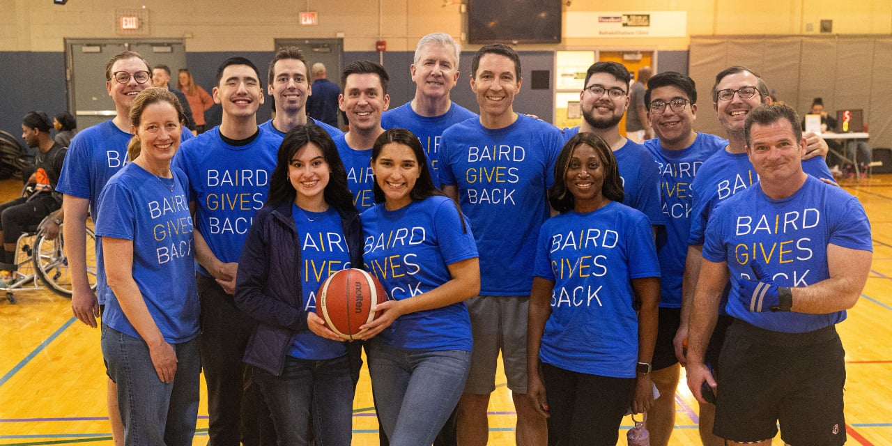 Baird Advisors associates posing with a basketball on a basketball court